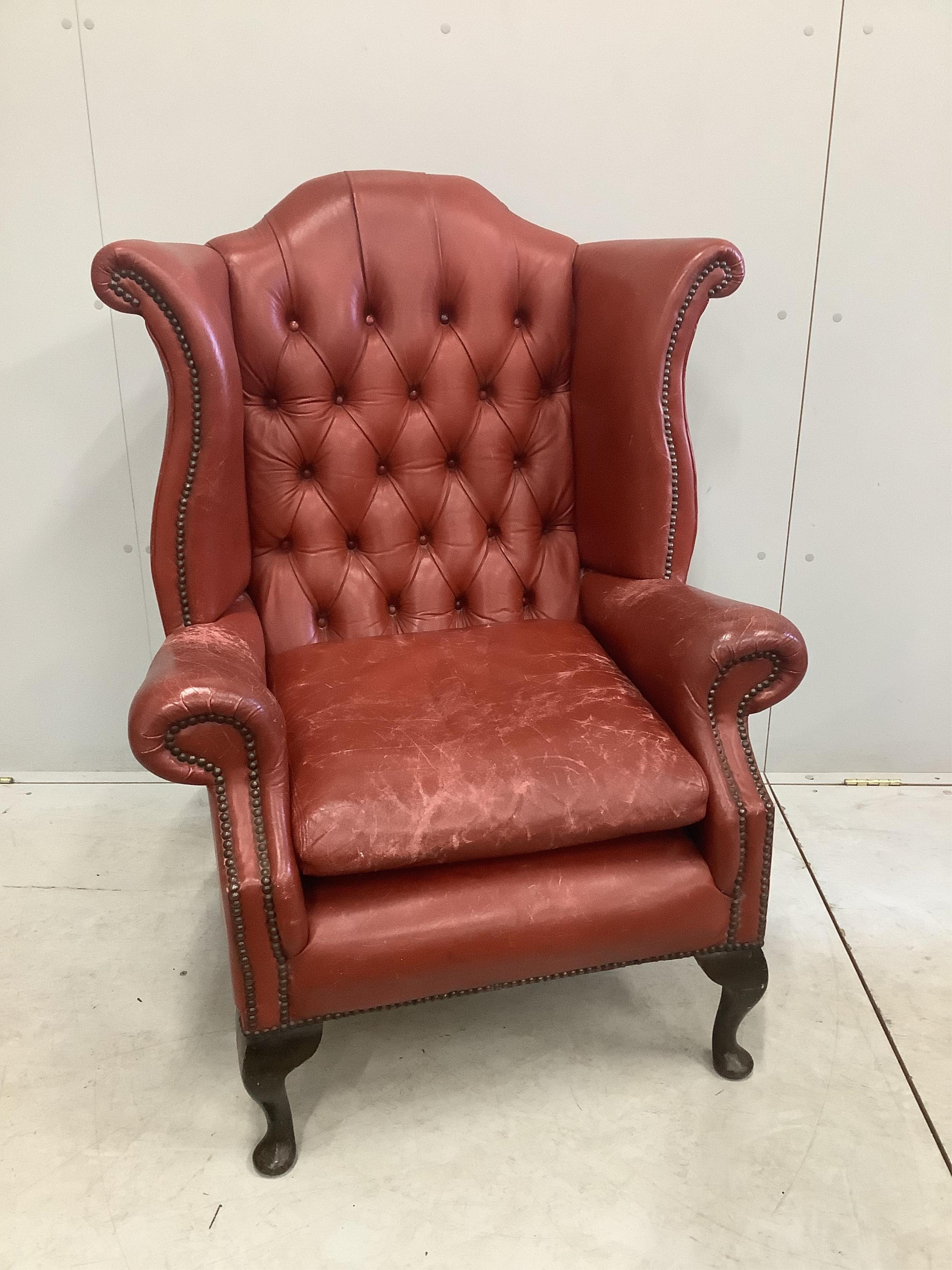 A Georgian style wing armchair with brick red leather upholstery, width 86cm, height 112cm. Condition - fair, but wear to the tops of the arms and seat